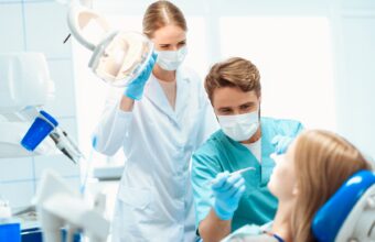 A dentist and a nurse are treating the patient. They stand over it in medical masks. They have medical instruments in their hands